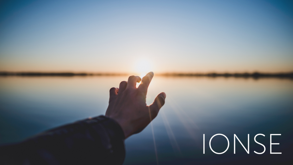 Foto de iones en la que se ve una mano tocando el sol en el horizonte.